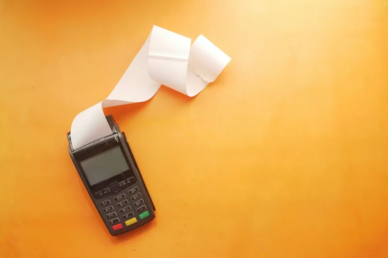 A payment terminal with a long paper receipt spilling out of it