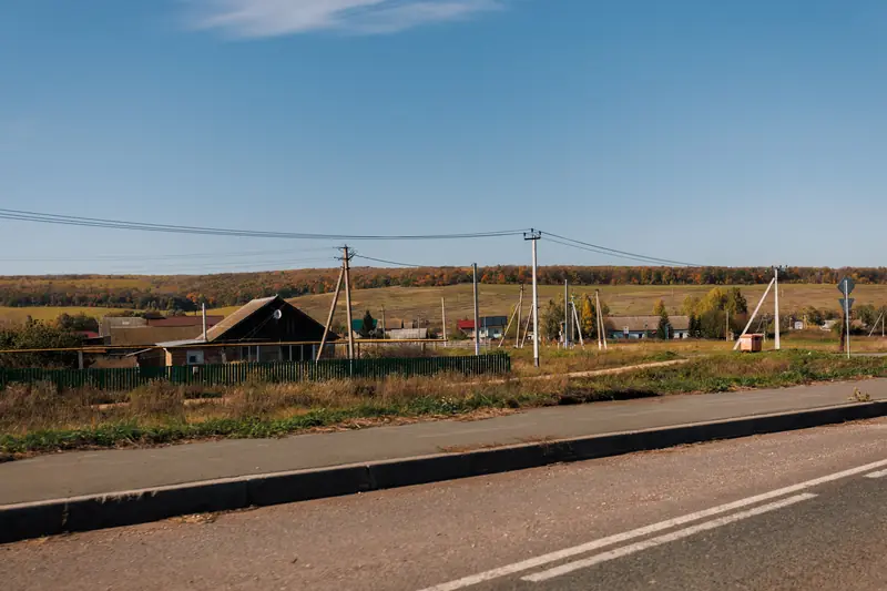 Utility poles and overhead lines running along a country road past a farmhouse and open fields